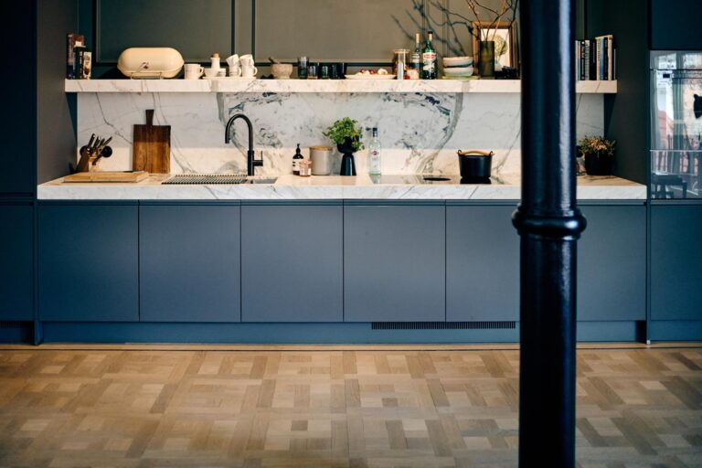 Parketvloer in blokpatroon in een moderne designkeuken met blauwe kasten en marmeren werkblad
